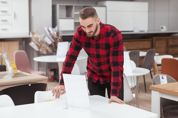 Atractivo joven examinando muebles a la venta en la tienda de muebles