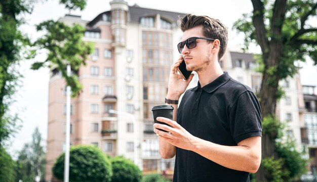 Atractivo joven con gafas de sol hablando por un teléfono inteligente en la ciudad