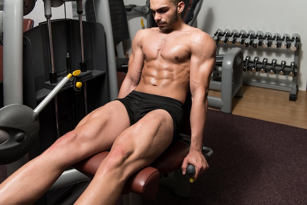 Atractivo joven haciendo ejercicios de piernas con máquina en el gimnasio