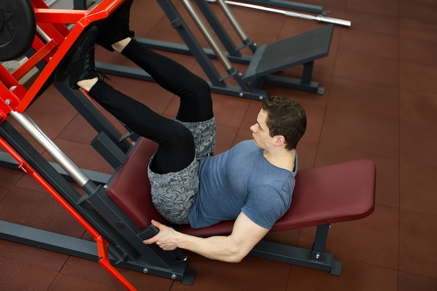 Atractivo joven haciendo prensa de piernas en la máquina en el gimnasio