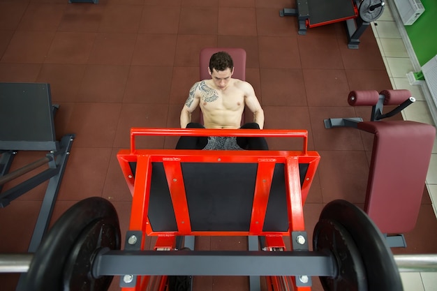 Foto atractivo joven haciendo prensa de piernas en la máquina en el gimnasio
