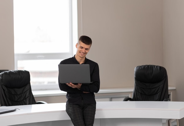 Atractivo joven en la oficina en una sala de conferencias con una computadora portátil en sus manos