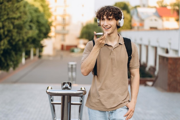 Atractivo joven universitario de pelo rizado o estudiante universitario con mensaje de voz grabado por teléfono en el campus