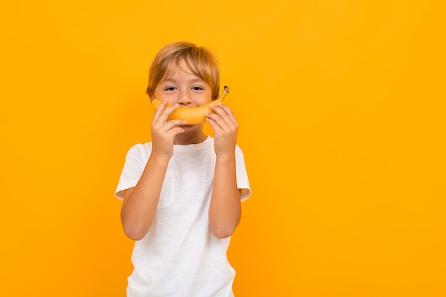 Atractivo muchacho europeo en una camiseta blanca con una banana en sus manos sobre una pared naranja