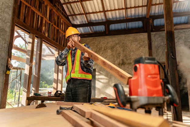 Atractivo trabajador carpintero masculino profesional de mediana edad mirando y eligiendo madera en la mesa de madera en el sitio de construcción.