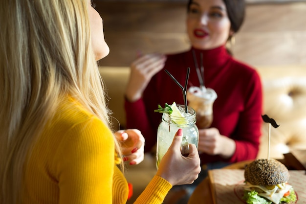 Atractivos amigos bebiendo cócteles juntos Dos hermosas mujeres jóvenes sentadas en el bar con bebidas