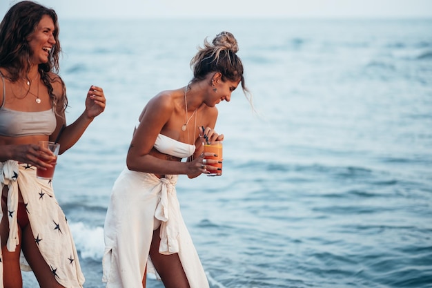 Atractivos amigos disfrutando de las vacaciones juntos en la playa y bebiendo cócteles