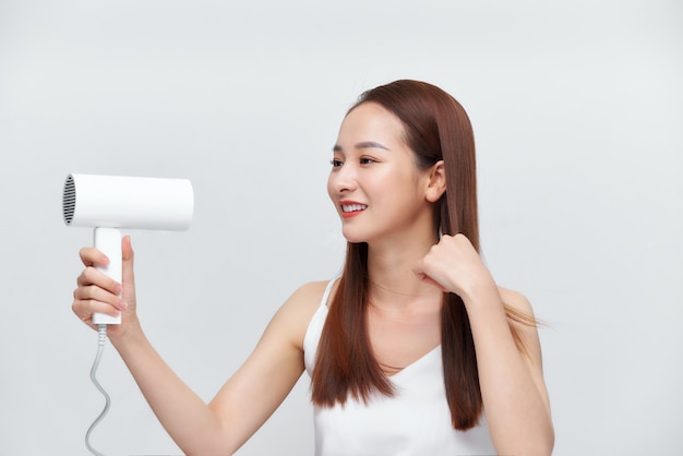 Atraente adolescente alegre seca o cabelo com secador, sobre branco