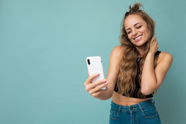Atraente charmosa jovem sorridente feliz segurando e usando telefone celular tirando selfie com roupas elegantes