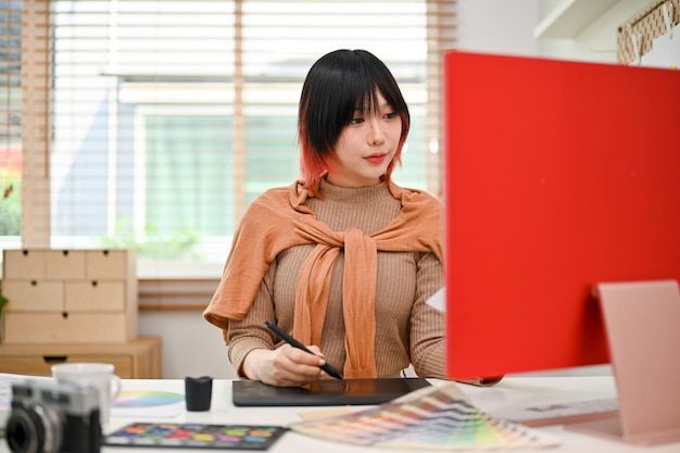 Atraente designer gráfico feminino asiático usando um tablet gráfico e computador