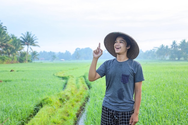 Atraente e alegre jovem agricultor asiático de pé e mostrando um momento aha tendo ideia do campo de arroz