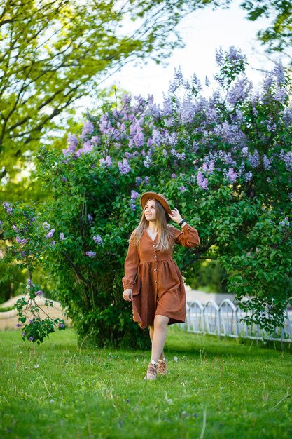 Atraente elegante sorridente magro garota com cabelo comprido anda no parque, vestida com um vestido marrom quente, moda outono na moda de rua, com um chapéu. Mulher jovem de aparência europeia
