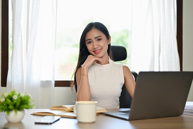 Atraente empresária asiática do milênio senta-se em sua mesa com a mão no queixo