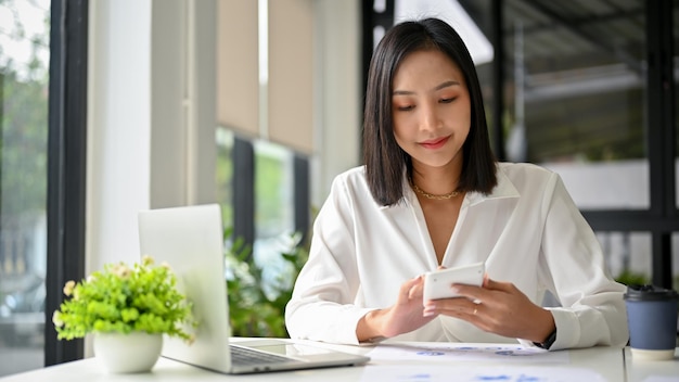 Atraente empresária asiática milenar usando calculadora para calcular vendas