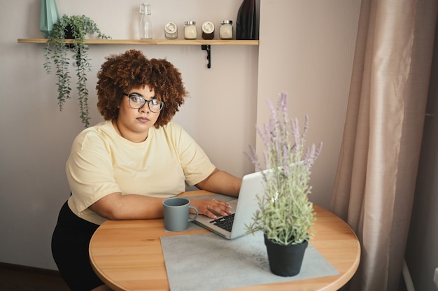 Atraente feliz elegante plus size estudante negra afro-americana de óculos estudando online