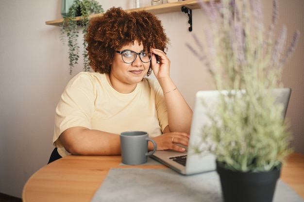 Atraente feliz elegante plus size estudante negra afro-americana de óculos estudando online