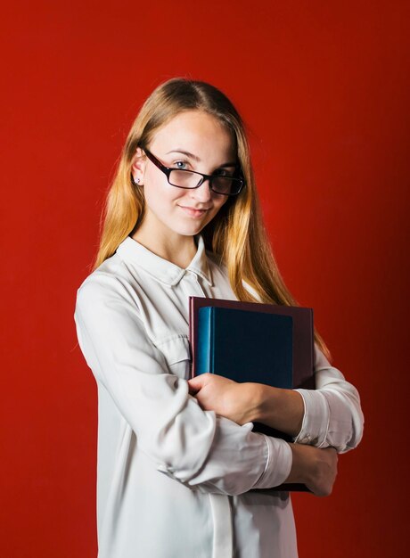 Atraente feliz sorridente estudante loira de camisa branca com livros sobre o conceito de estudante de fundo vermelho