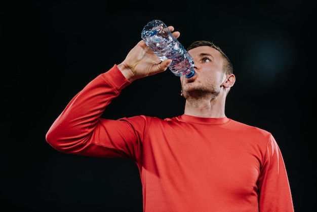 Atraente jovem desportista caucasiano bebendo água da garrafa olhando para longe com expressão de rosto pensativo vestido com roupas esportivas vermelhas relaxando após corrida ou treino Motivação esportiva Estilo de vida