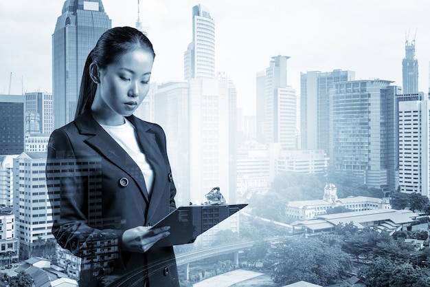 Atraente jovem empresária asiática de terno tomando notas no caderno novas oportunidades de carreira atribuição de MBA Kuala Lumpur em segundo plano Dupla exposição