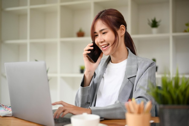 Atraente jovem empresária asiática falando ao telefone com parceiro de negócios