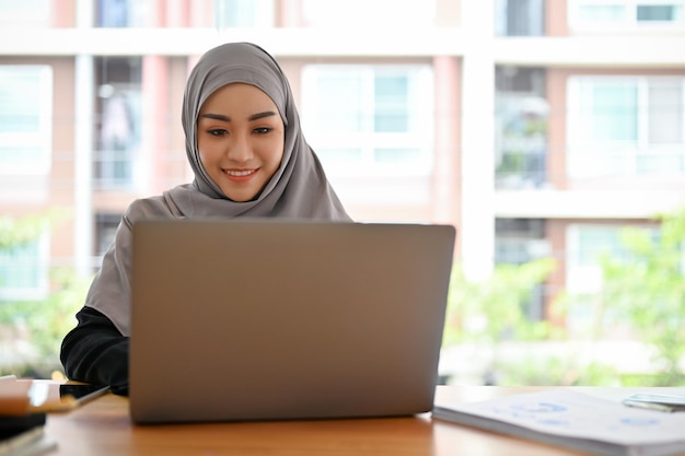 Atraente jovem empresária muçulmana com hijab na reunião no laptop portátil