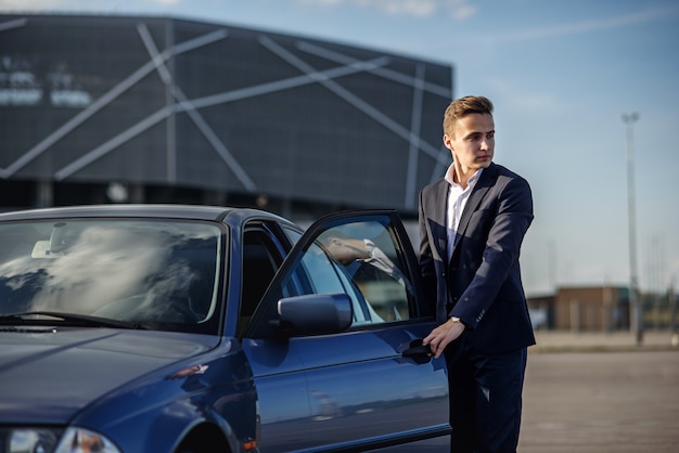 Atraente jovem empresário bem sucedido em um terno de negócio abre a porta do seu carro