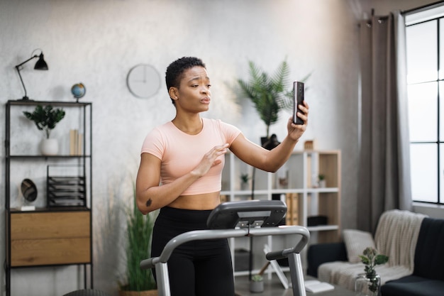 Atraente jovem esportiva africana fazendo videochamada online enquanto malha