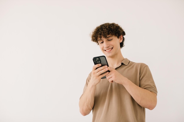 Atraente jovem estudante do sexo masculino usando o telefone em um fundo branco com espaço livre