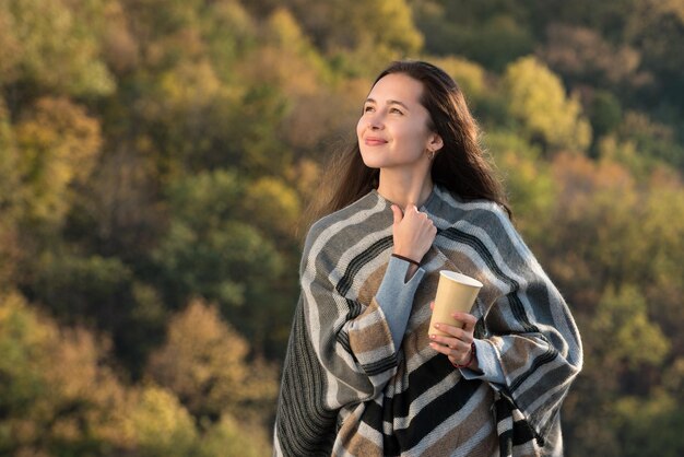 Atraente jovem morena em um poncho com um café na mão Garota olha para o céu e sorrindo