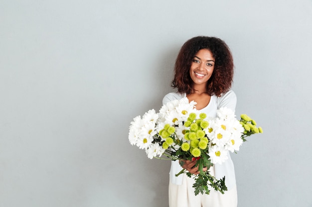 Atraente jovem mulher africana dando buquê de flores para camrera