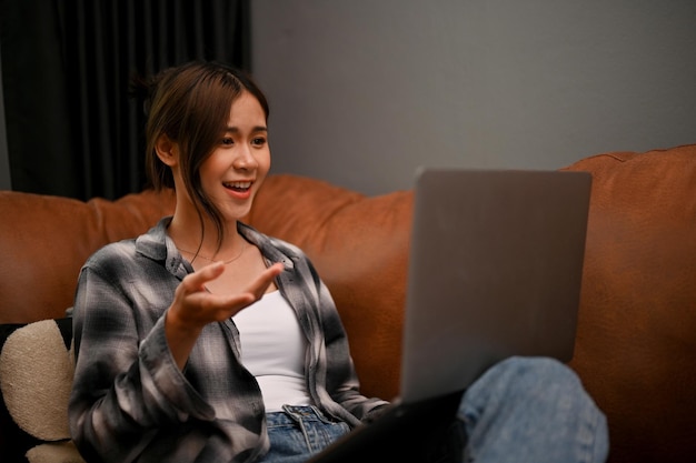 Atraente jovem mulher asiática gosta de conversar com seus amigos em uma chamada de vídeo através de seu laptop
