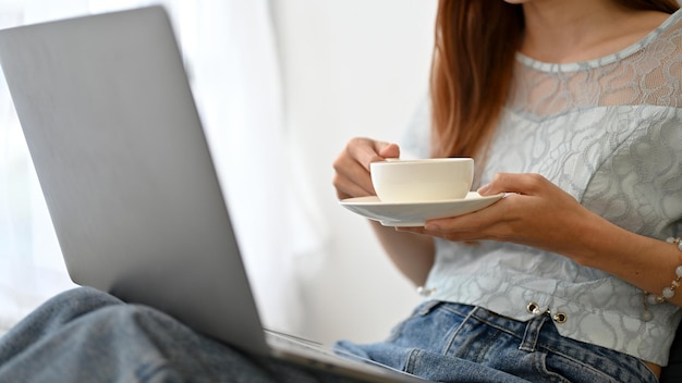 Atraente jovem mulher asiática usando laptop enquanto toma um café quente