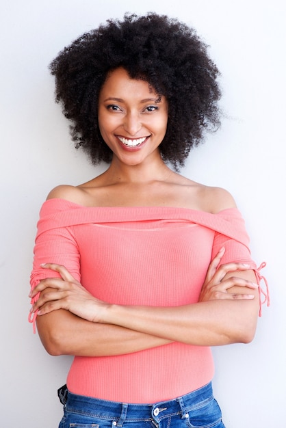 Atraente jovem negra em pé com os braços cruzados e sorrindo contra fundo branco