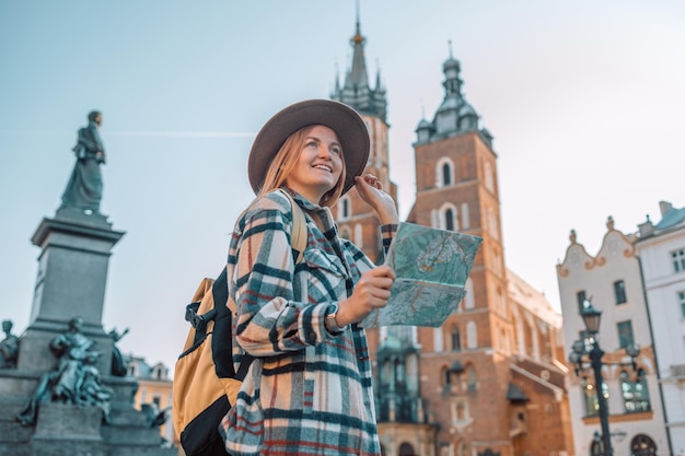 Atraente jovem turista está explorando a nova cidade Garota de chapéu segurando um mapa de papel na Praça do Mercado em Cracóvia Viajando pela Europa em um dia ensolarado no outono Foto de alta qualidade