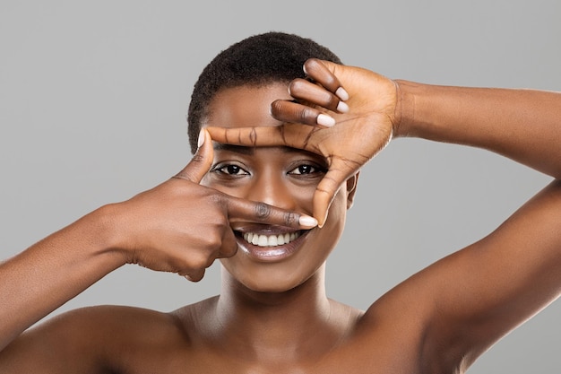 Atraente mulher afro emoldurando seus lindos olhos com os dedos