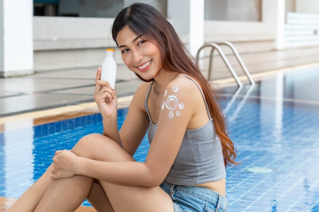 Atraente mulher asiática segurando uma garrafa de protetor solar e aplicar protetor solar em forma de sol UV proteger ao ombro.