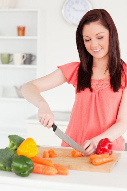 Atraente mulher ruiva cortando algumas cenouras na cozinha