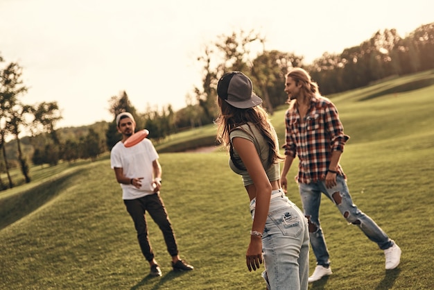 Foto ¡atrapa el frisbee! grupo de jóvenes en ropa casual lanzando discos de plástico mientras pasan tiempo sin preocupaciones al aire libre