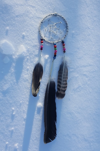 Foto atrapasueños sobre fondo de nieve. decoración artesanal con plumas y abalorios de colores.