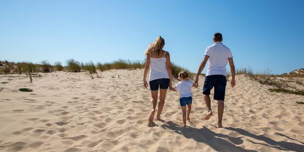 Atrás da família pai mãe e filha criança vista traseira na praia no mar andando na areia