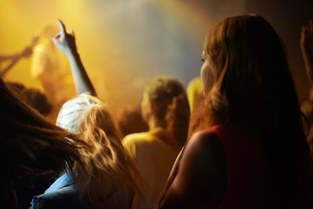 Atrás da mulher na multidão fã no show ou festival de música assistindo evento de rock no palco Garota na platéia entusiasmou os fãs na apresentação da banda ao vivo na arena ou estádio com luzes e energia no show noturno