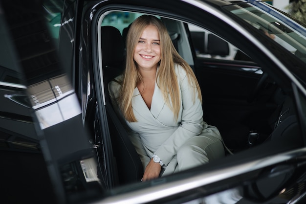 Attactive bussines joven mujer sentada en el coche en la sala de exposición de coches mujer eligiendo coche nuevo hermosa rubia