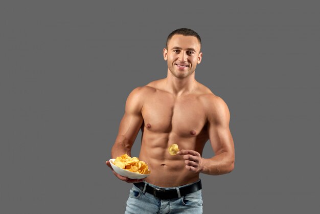 Attactive homem sorrindo, segurando a tigela com batatas fritas.