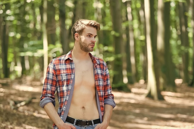 Attraktiv und charismatisch Sexy Mann steht in Holz auf Naturlandschaft Schöner Kerl mit sexy nacktem Oberkörper im offenen Hemd Sommerurlaub Fernweh und Reisen