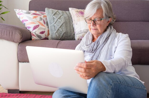 Attraktive ältere Frau zu Hause, die auf dem Boden unter Verwendung einer Laptop-Computer sitzt. Ein älterer Rentner, der Freizeit und technische Geräte genießt