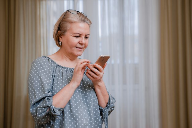 Attraktive ältere Geschäftsfrau mit einem lächelnden Mobiltelefon, als sie über Videolink auf den Bildschirm schaut