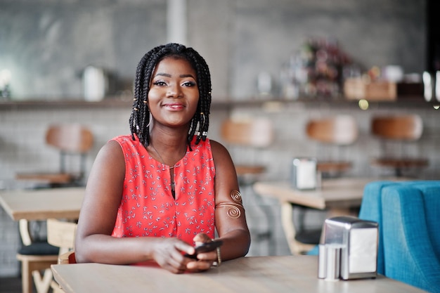 Attraktive afrikanisch-amerikanische Frau sitzt am Tisch im Café mit Handy in der Hand