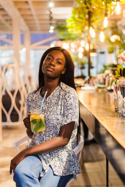 Attraktive afrikanische Frau, die im Café sitzt und frische Limonade trinkt.