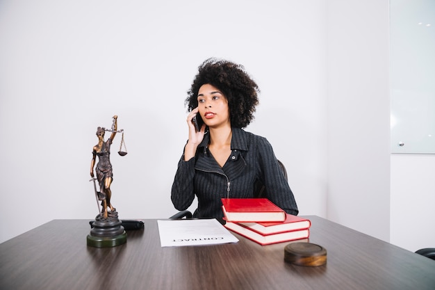 Foto attraktive afroamerikanerfrau, die bei tisch am handy im büro spricht