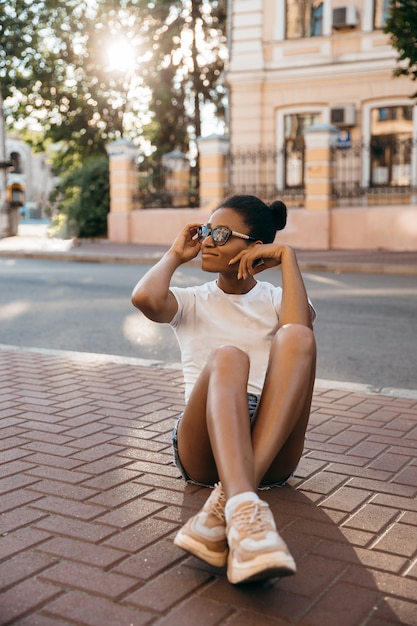 Attraktive afroamerikanische Frau, die auf dem Stadtstraßenplatz auf Sonnenuntergang sitzt